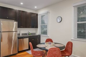 A modern kitchen with dark cabinets, stainless steel appliances, and a dining area with red chairs and a round table.