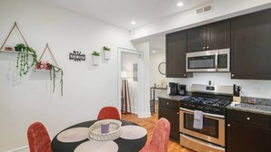 A modern kitchen with dark cabinets, stainless steel appliances, and a dining area with a round table and red chairs.
