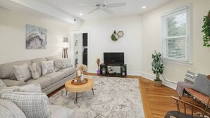 A living room with a sofa, a coffee table, a TV, a ceiling fan, and a window with blinds.