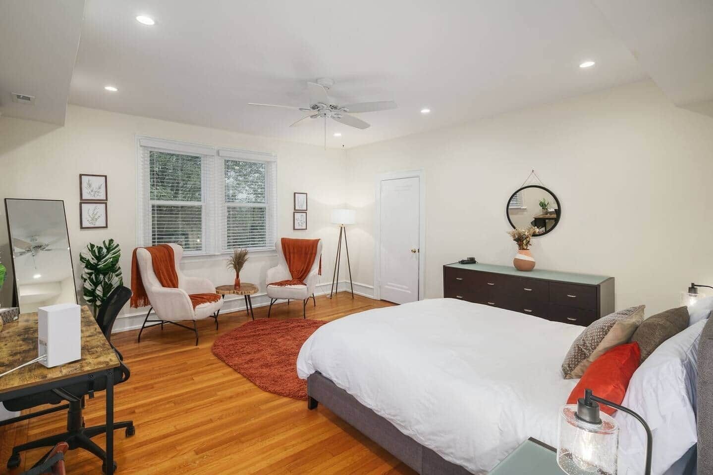 A bedroom with a bed, desk, chair, bedside table, and a ceiling fan.
