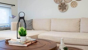 A modern living room with a beige sofa, two wooden coffee tables, a small potted plant, and decorative wall art.