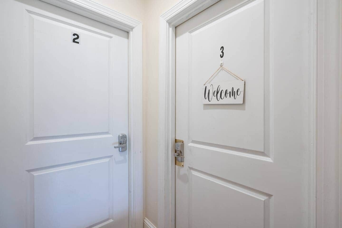 Deux portes blanches, portant les numéros 2 et 3, et une pancarte « Bienvenue » sur la porte numéro 3.