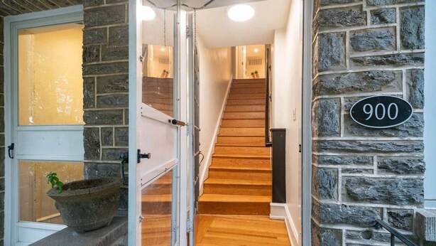 A stone exterior wall with a number plate reading '900', a wooden staircase, and a door with glass panels.