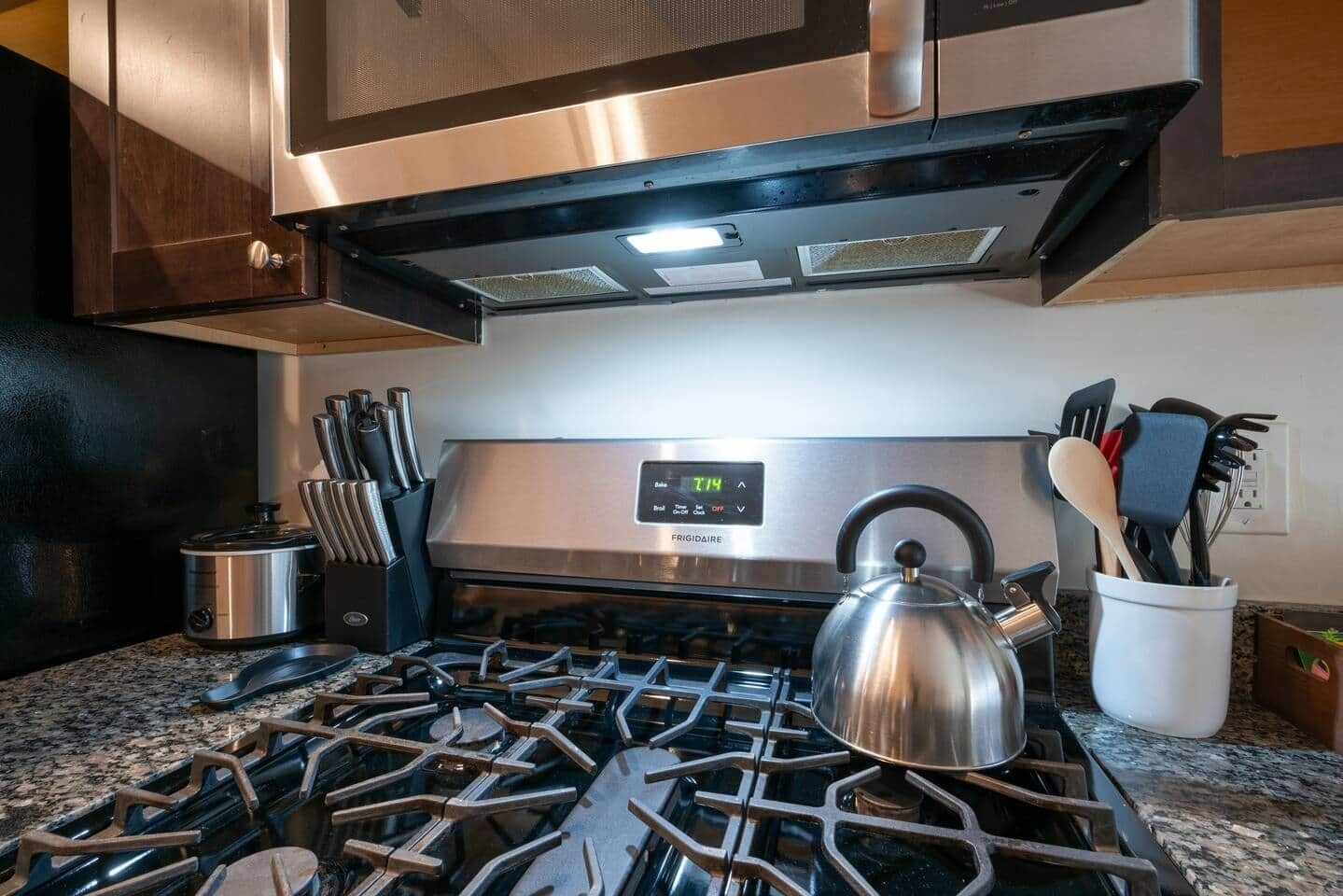 Una cocina con estufa de acero inoxidable, hervidor y un juego de cuchillos.