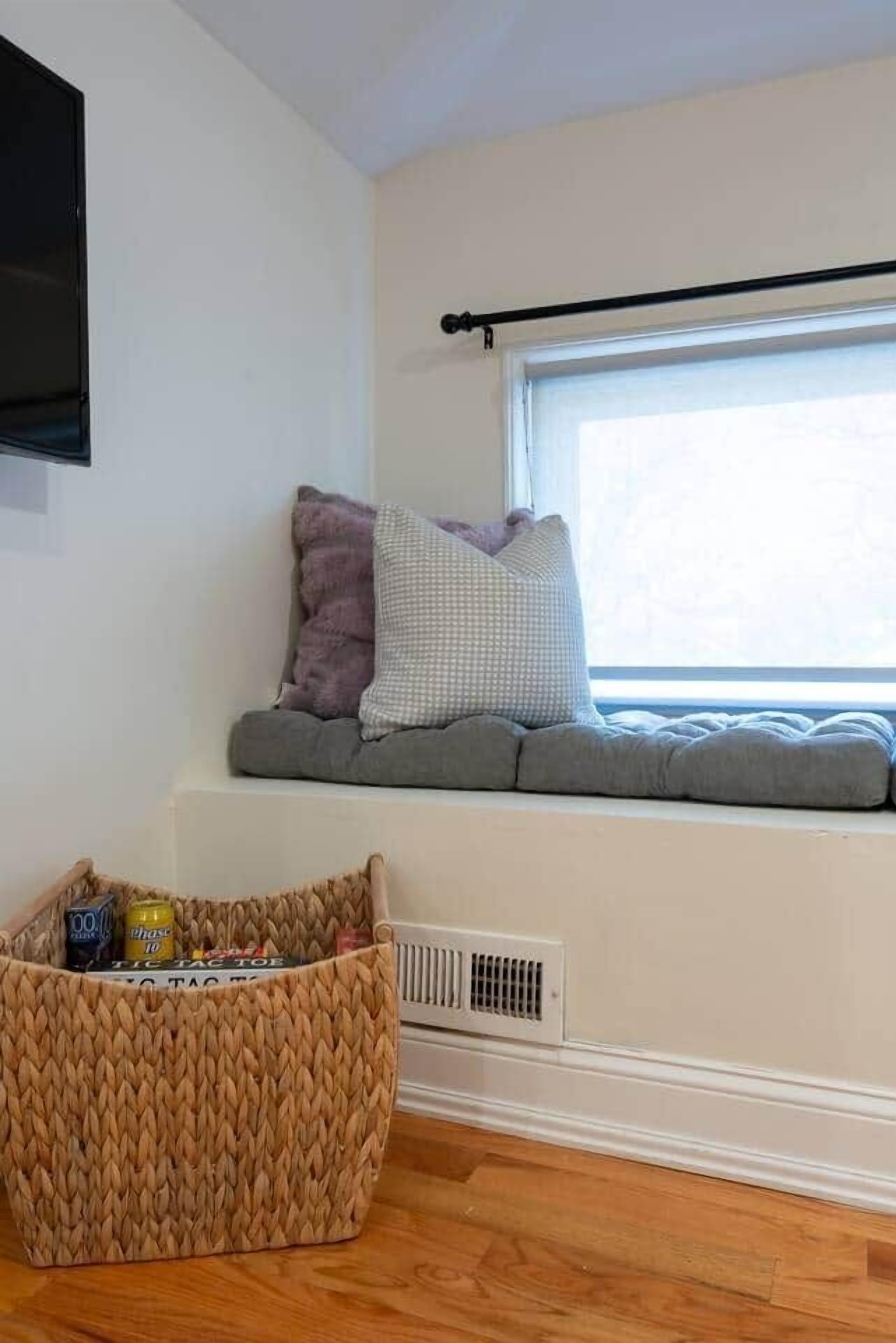 A room with a window seat, a woven basket, and a mounted television.