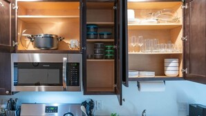 A kitchen with a built-in microwave, a stove, and open cabinets revealing storage shelves and kitchenware.