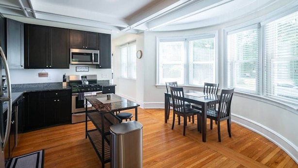 A modern kitchen with dark cabinets, a microwave, and a stove. There is a dining area with a table and chairs.