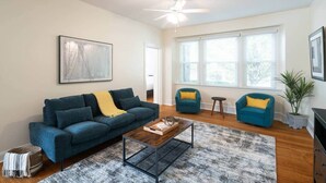 A living room with a sofa, two armchairs, a coffee table, a ceiling fan, and a large window.