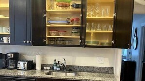 Une cuisine avec des meubles de couleur sombre, un plan de travail en granit, un lave-vaisselle, une machine à café et un évier.