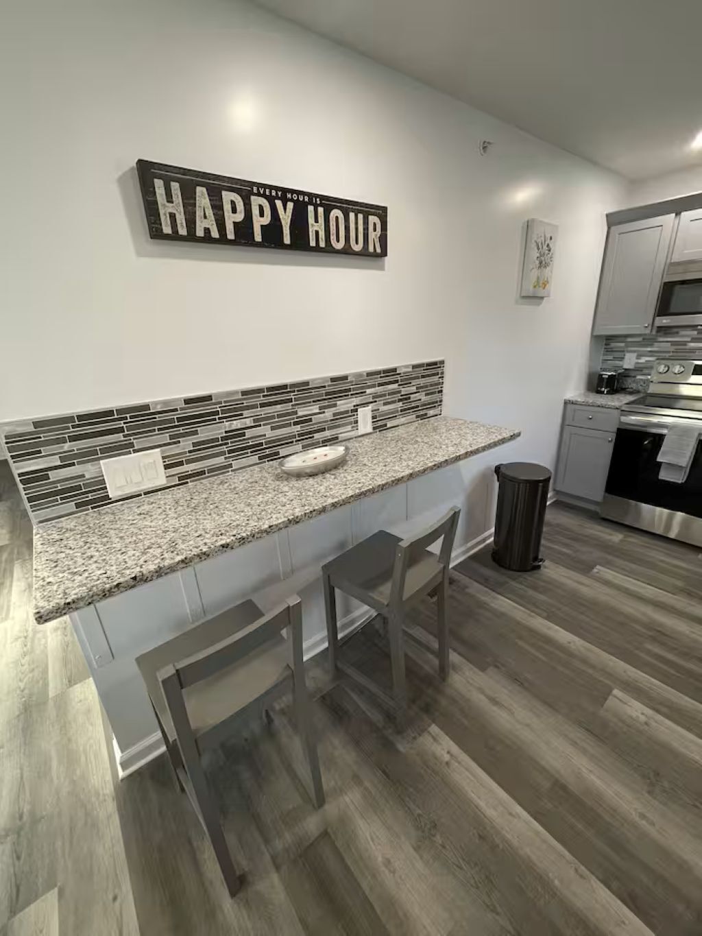 A modern kitchen with a granite countertop, two bar stools, a stainless steel oven, and a backsplash with mosaic tiles.