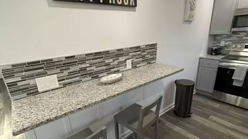 A modern kitchen with a granite countertop, two bar stools, a stainless steel oven, and a backsplash with mosaic tiles.