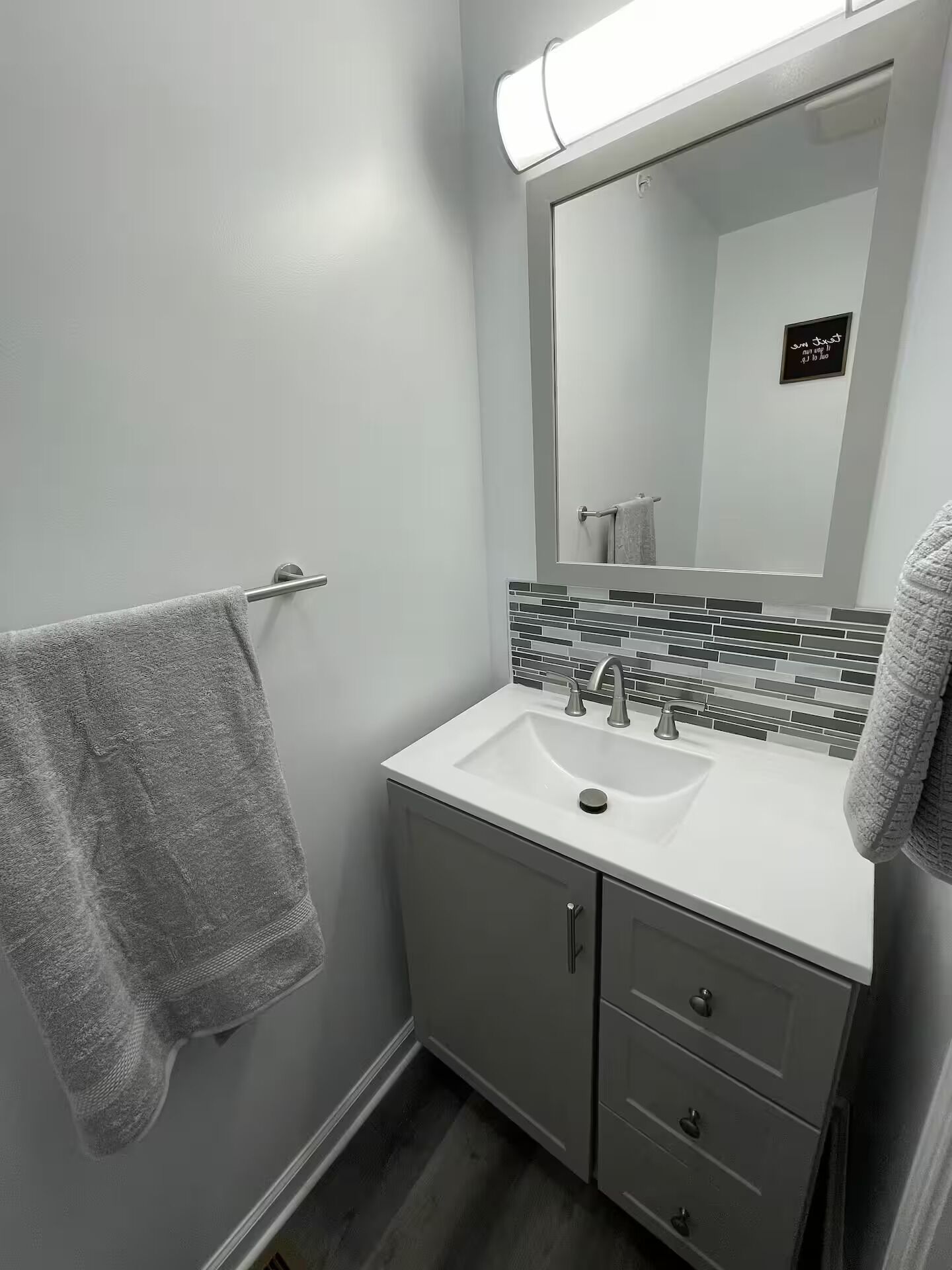 A bathroom with a white sink, a mirror with a black sign, and a towel rack.