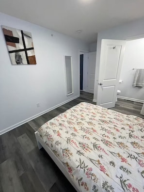 Un dormitorio con una cama, una puerta, una obra de arte colgada en la pared y un pasillo que conduce a otra habitación.