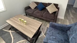 A living room with a sofa, a coffee table, a patterned armchair, a painting, and a framed word on the wall. - 2-bedroom apartment in excellent Newburgh with AC and charm (Newburgh)