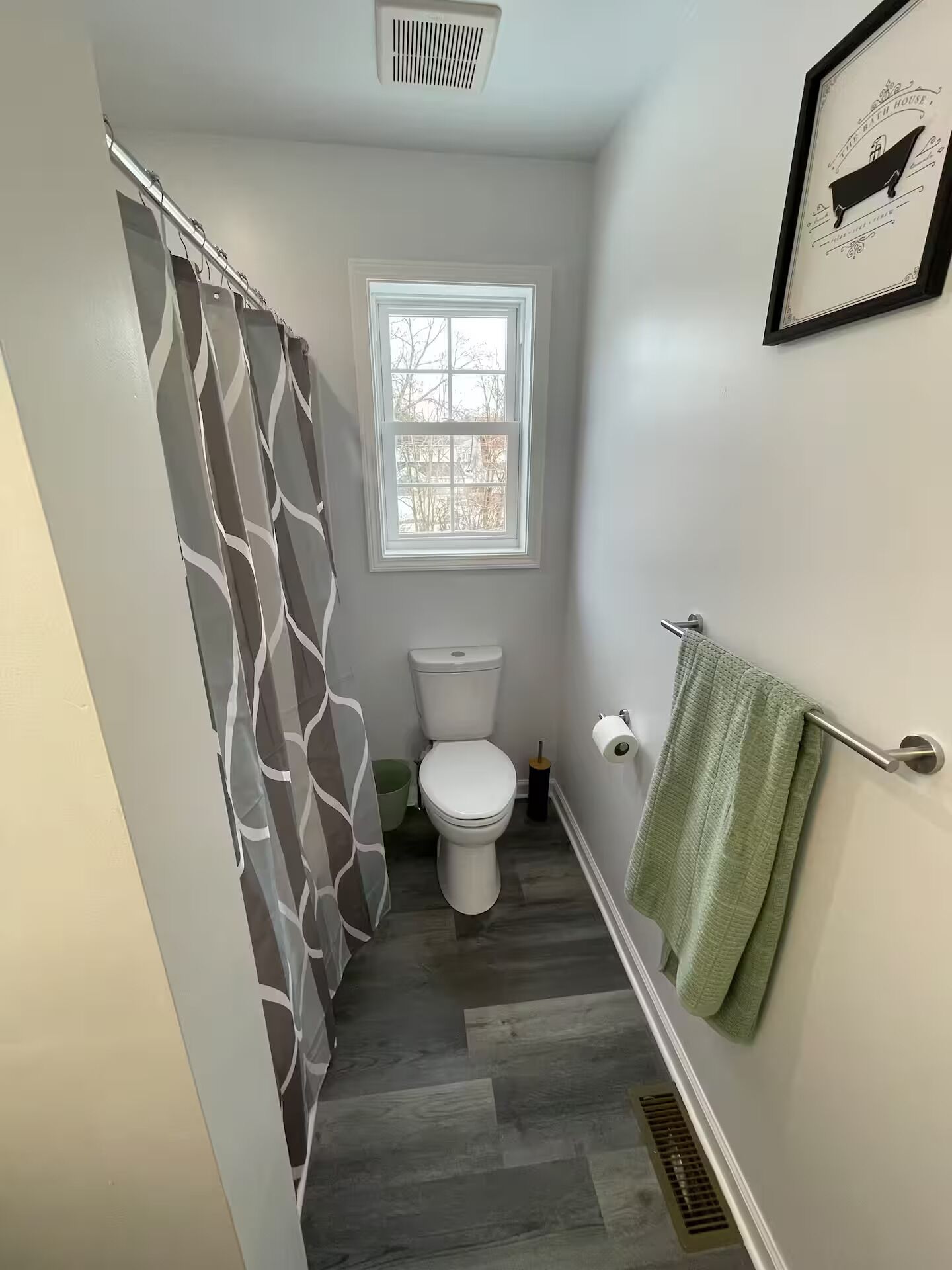 A bathroom with a toilet, a window, a shower curtain, and a towel rack.