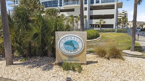 A sign for the Emerald Dolphin Hotel, featuring a dolphin logo and the address 850 North Mickey Mouse Road. - "Heaven on Top" – 15th-Floor Gulf Views, Pool & Hot Tub , Steps to Beach (Pensacola Beach)