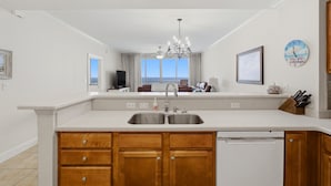 A kitchen with a double sink, wooden cabinets, a chandelier, and a view of the outdoors. - "Heaven on Top" – 15th-Floor Gulf Views, Pool & Hot Tub , Steps to Beach (Pensacola Beach)