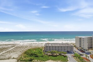 Un hotel frente al mar con vistas a la playa, varios pisos y un estacionamiento.
