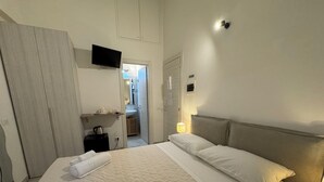 A hotel room with a bed, a TV mounted on the wall, a bedside lamp, and a door leading to a bathroom. - Bosuites Rome (Rome)