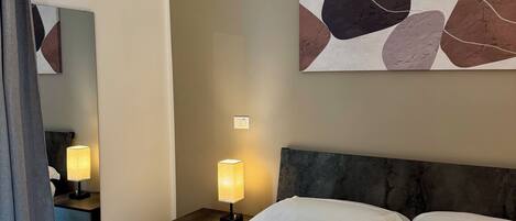 A hotel room with a bed, two bedside lamps, a large abstract painting, and a mirror.