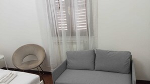 A room with a grey sofa, a round chair, a white table, and a window with blinds. - Vibes Pigneto, central location near metro C stop suitable for families (Roma)