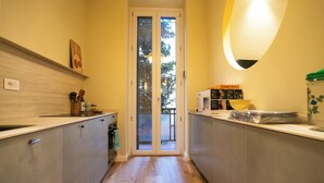Eine schmale Küche mit einer Schiebetür zum Balkon, Holzboden und einer Arbeitsfläche mit Küchenutensilien und Geräten.