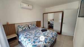 A bedroom with a bed, bedside tables, a wardrobe, and an air conditioning unit. - Apartamento Aconchego do Ribeirão - FLN (Florianópolis)