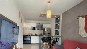 A modern kitchen with white cabinets, a built-in oven, and a dining area with a red sofa and black chairs. - Apartamento Aconchego do Ribeirão - FLN (Florianópolis)