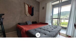 A bedroom with a bed, a window with a view, and a macrame wall hanging. - Apartamento Aconchego do Ribeirão - FLN (Florianópolis)