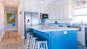 A modern kitchen with white cabinets, a blue island, stainless steel appliances, and a map on the wall. - Intracoastal Sanctuary 2BR 2BA in Sabine Pass (Sabine Pass)