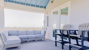 A covered outdoor area with a light-colored sofa and Adirondack chairs, a wooden deck, and a view of the horizon. - Intracoastal Sanctuary 2BR 2BA in Sabine Pass (Sabine Pass)