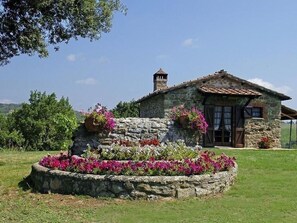 A stone house with a tiled roof, a chimney, and a flower bed with pink flowers. - Antico Casale San Lorenzo (Toscana)