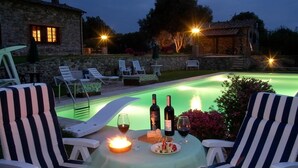 A poolside setting with lounge chairs, a table with wine bottles and glasses, and a candle. - Antico Casale San Lorenzo (Toscana)