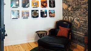 Une pièce avec un plancher en bois, un tapis vert, un fauteuil en cuir noir et un mur orné de posters encadrés.