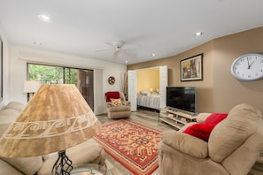 A living room with a sofa, a TV, a clock, and a door leading to another room. - CASA MIDDIE-Two Bedroom with the best View (Phoenix, Arizona)