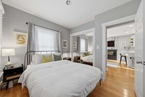 Ein modernes Schlafzimmer mit einem großen Bett, Nachttischen, einer Lampe und Blick in den Wohnbereich.