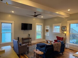 A living room with a ceiling fan, a flat-screen TV, a fireplace, and a large window. - Cromwell House- A historic, restored 4-bedroom home in beautiful South Frankfort (Frankfort)