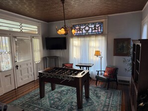 A room with a foosball table, a television, a chandelier, and a patterned rug. - Cromwell House- A historic, restored 4-bedroom home in beautiful South Frankfort (Frankfort)