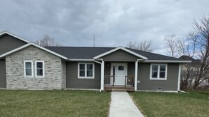 A two-story house with a stone facade, a front porch, and a driveway leading to the entrance. - Cozy East Duplex (Seymour)