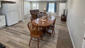 A spacious living area with a dining table and chairs, a sofa, and a kitchen with white cabinets and appliances. - Cozy East Duplex (Seymour)