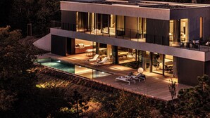 Ett modernt hus i två våningar med en swimmingpool, en uteplats och en stor glasfasad.