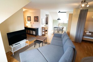 Una sala de estar moderna con una televisión de pantalla plana, un sofá gris y un comedor con una mesa y sillas.