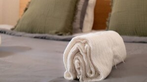 A neatly made bed with a rolled white towel, two green pillows, and a wall-mounted lamp. - Harbor-View Loft | 2BR Near City (Gothenburg)