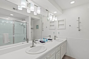 Ein modernes Badezimmer mit zwei Waschbecken, einer Duschkabine aus Glas und einem großen Spiegel.