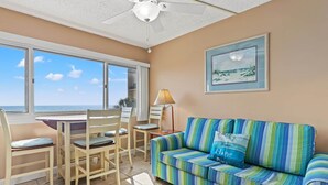 Ein Zimmer mit Meerblick, ein gestreiftes Sofa, ein Esstisch mit Stühlen und ein Deckenventilator.