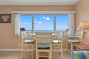 Une pièce avec vue sur l’océan, une table ronde entourée de chaises, une lampe et un tableau accroché au mur.