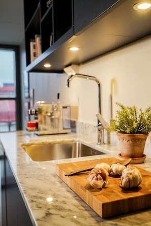 Una cocina moderna con encimera de mármol, tabla de madera con ajos, planta en maceta y pileta de acero inoxidable.
