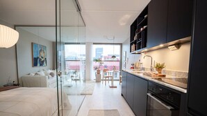 Ein modernes Apartment mit einer Glasabtrennung, die Wohnbereich von der Küche, einem Essbereich und einem Balkon mit Stadtblick trennt.