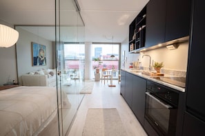 Un apartamento moderno con un separador de vidrio que divide la sala de estar de la cocina, un comedor y un balcón con vista a la ciudad.