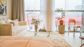 Ein modernes Wohnzimmer mit einer Couch, einem Glastisch und Blick auf die Stadt durch große Fenster.